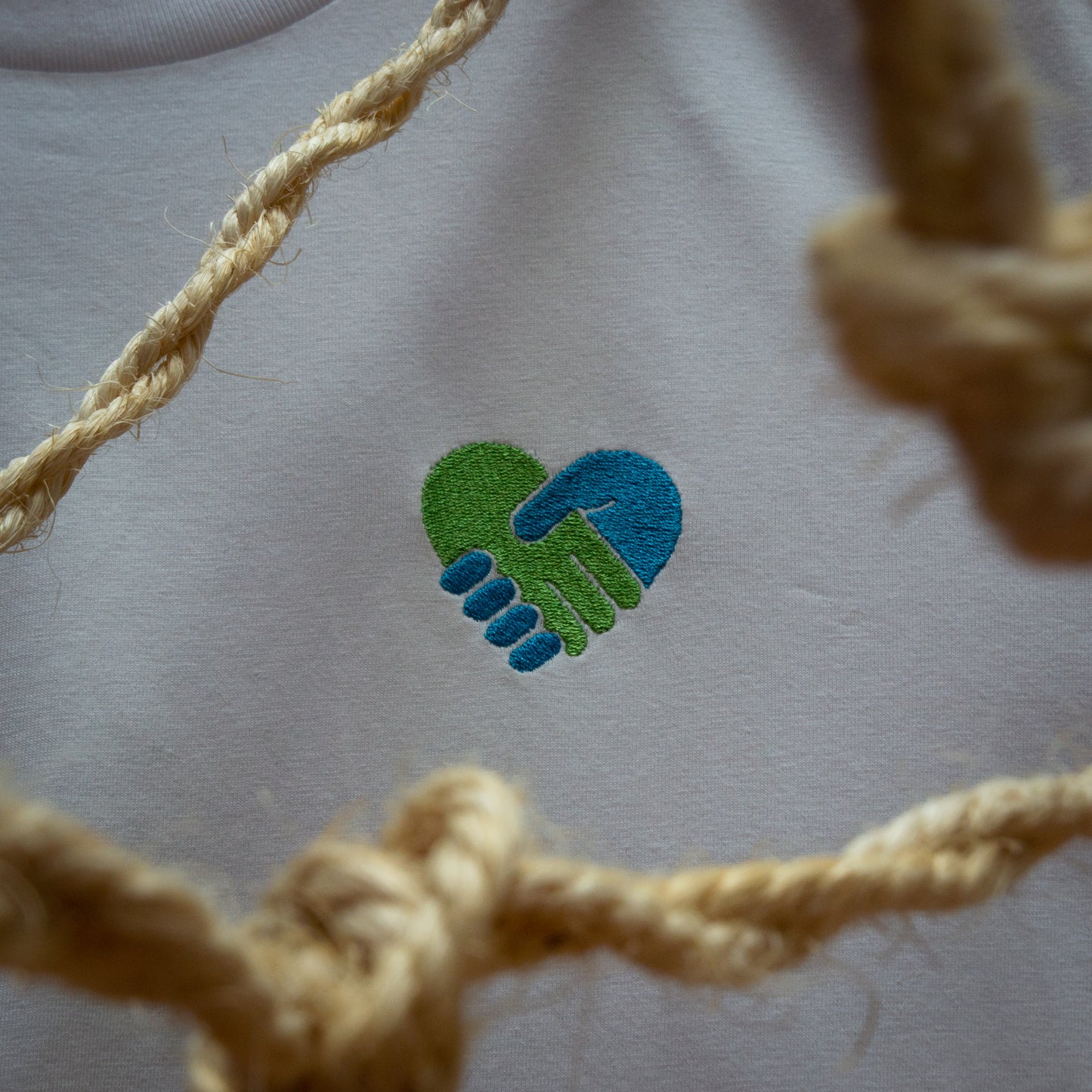 Close-up of the COMMUNITY design with an embroidered design of two hands shaking surrounded by rope