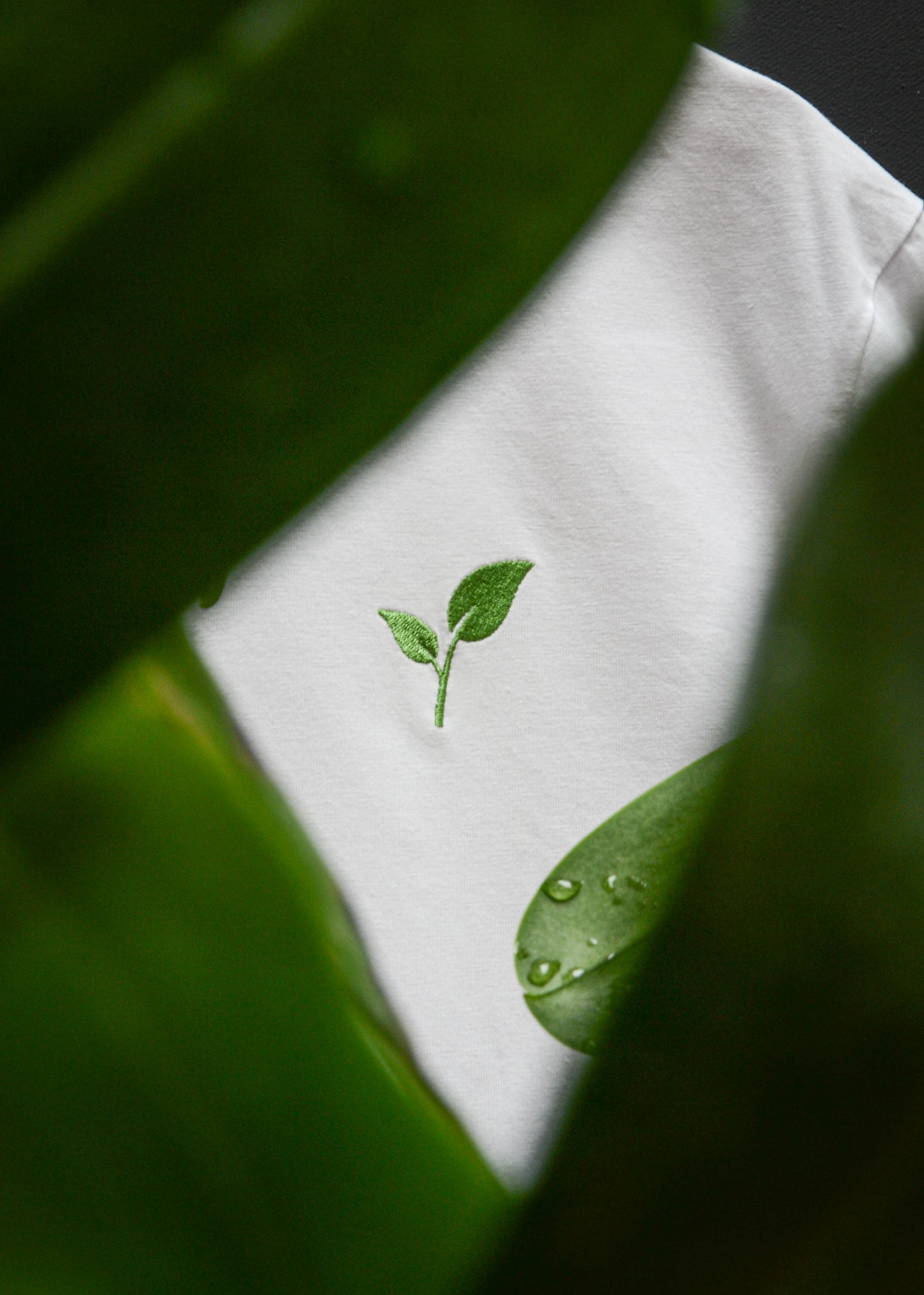 Close-up of GROWTH design with an embroidered green sapling design with leaves in the foreground