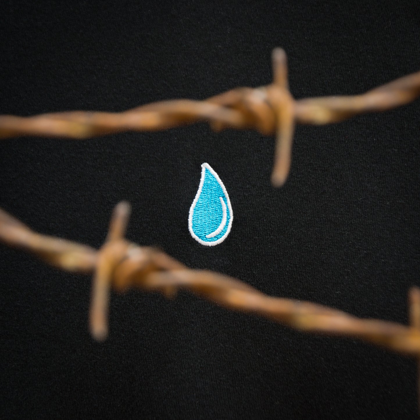 Close-up of the LOUD GAZE design with an embroidered tear drop surrounded by barbed wire